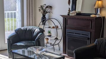 Un salon comprenant un fauteuil en cuir, une table basse en verre, une cheminée et une étagère décorative en métal.