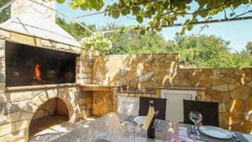 An outdoor dining area with stone walls, a grill, and a table set for two.