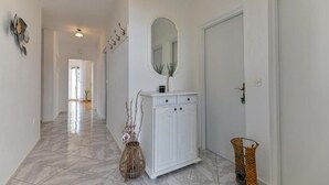 Un couloir avec une armoire blanche, un miroir et un vase décoré de branches.