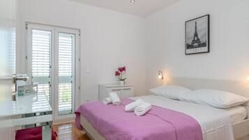 A bedroom with a bed, a desk, a chair, a nightstand, a picture of the Eiffel Tower, and a door with blinds.