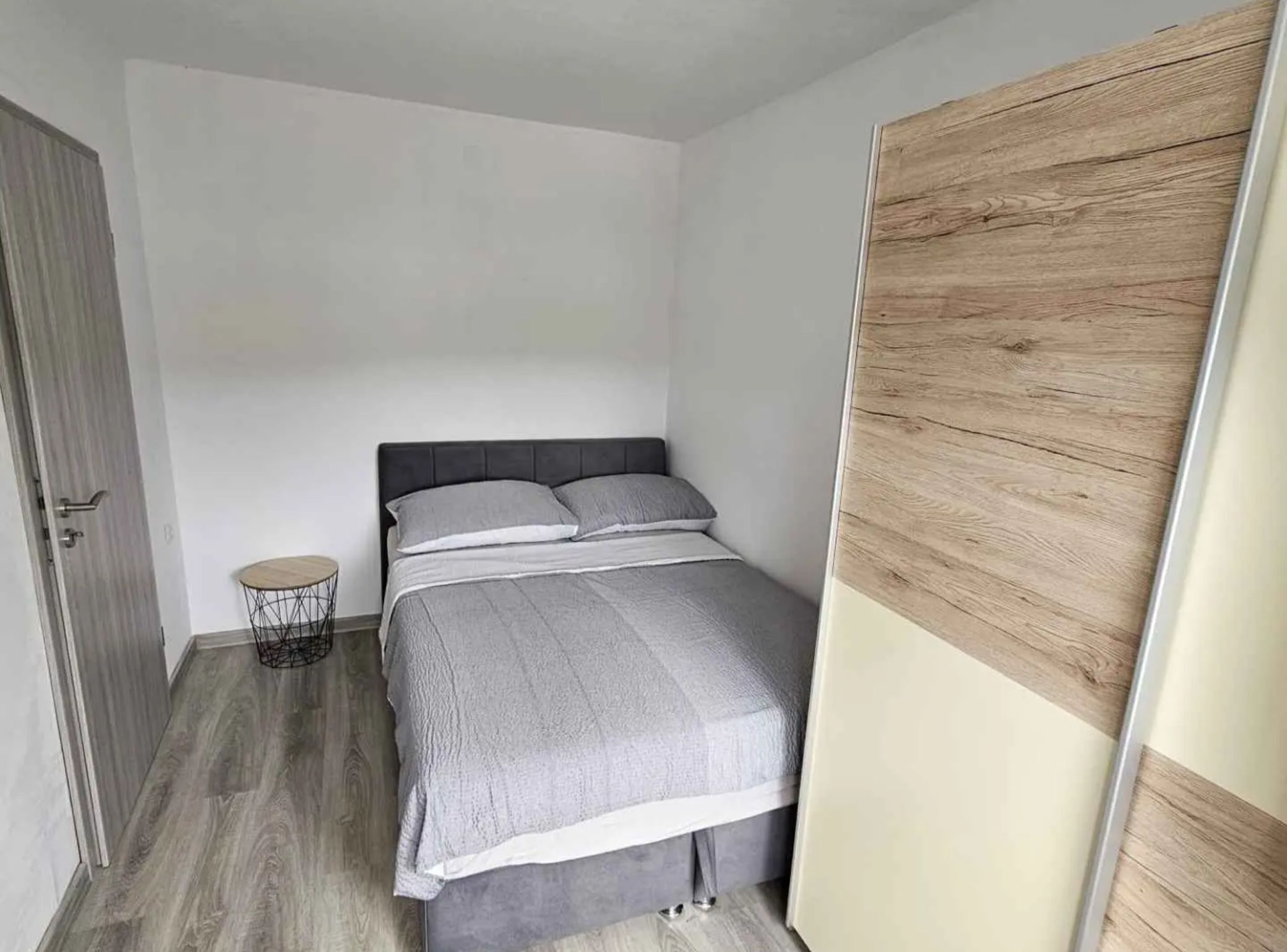 A small, modern bedroom with a bed, a small round table, and a wardrobe.