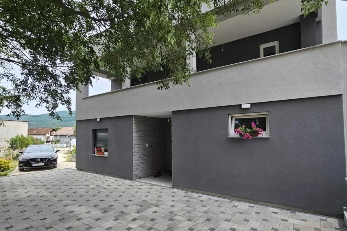 Ein modernes, zweistöckiges Gebäude mit grauer Fassade, einem kleinen Fenster mit Blumen und einem geparkten Auto auf der Auffahrt.