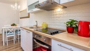 A modern kitchen with a built-in stove, a sink, and a stainless steel range hood. There is a dining area with a white table and chairs. - Apartment Sabo (Rijeka)