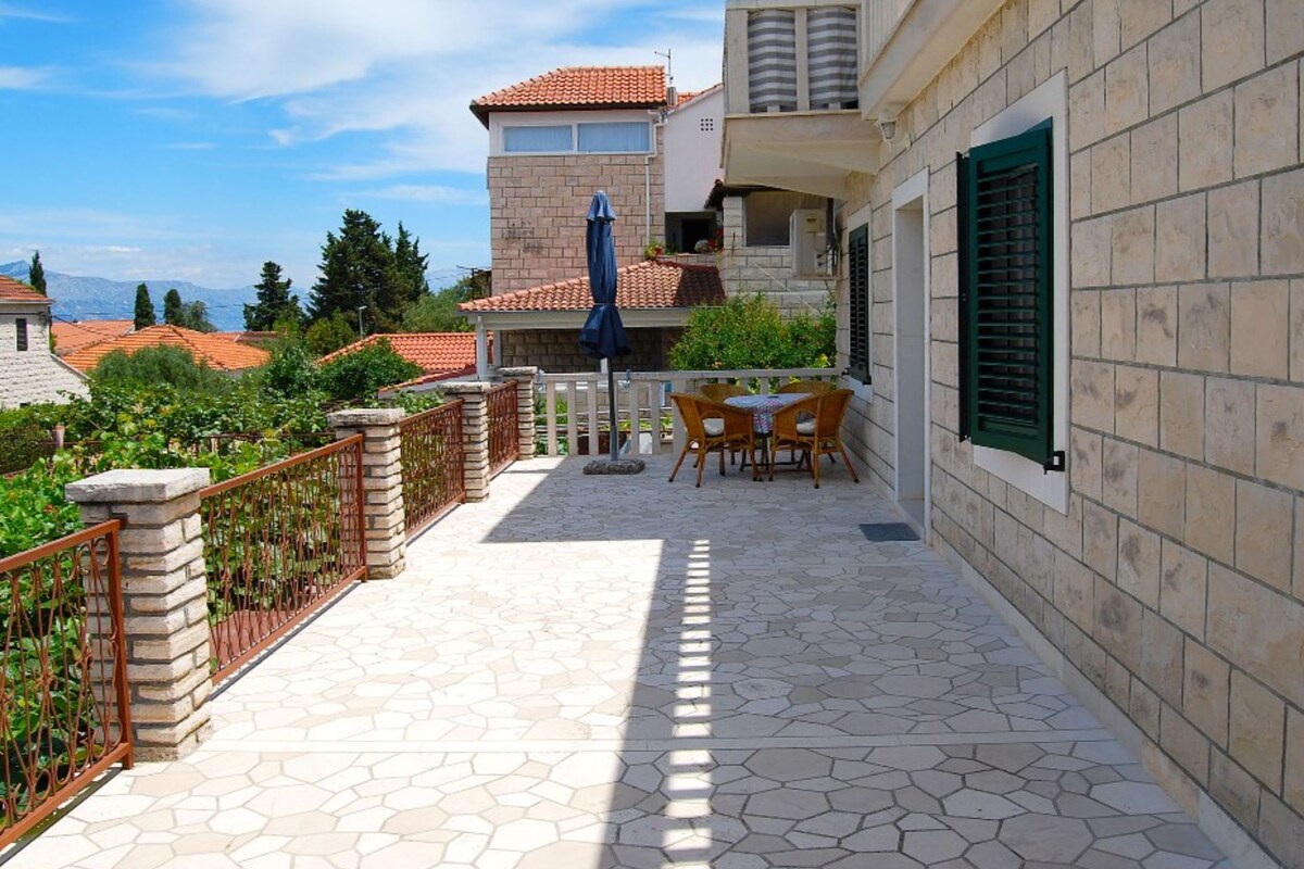 A patio with a table and chairs, a blue umbrella, and a stone wall.