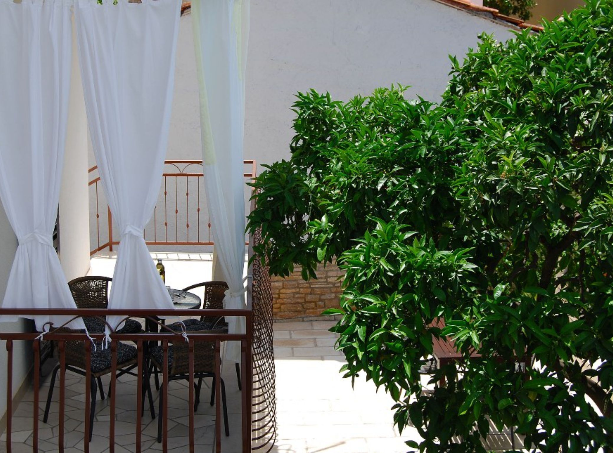 A patio with a table and chairs, a white curtain, and a green bush.