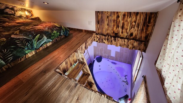 Una habitación con piso de madera, una bañera grande y una pared con un estampado de hojas tropicales.