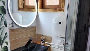 Un baño con tocador de madera, espejo redondo, ventana pequeña y cabina de ducha de vidrio.