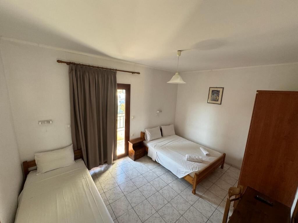 Une chambre à coucher avec un lit, une table de chevet, une lampe, une fenêtre avec des rideaux et une porte.