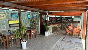Un’area salotto esterna coperta con pareti in pietra, tavoli e sedie in legno.