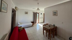 Una stanza con un letto, un divano rosso, un tavolo da pranzo con sedie e una ventola a soffitto.