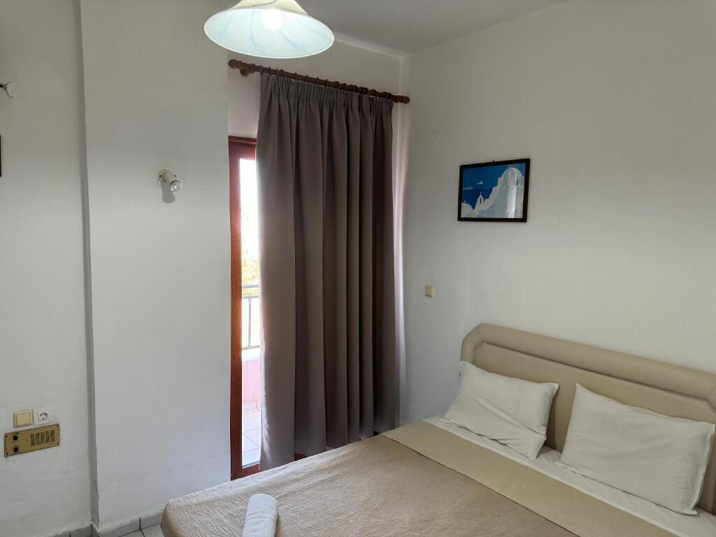 A bedroom with a bed, a window with curtains, a wall-mounted light fixture, and a framed picture.