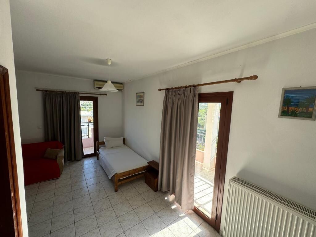Una habitación con una cama, un sofá rojo, una ventana con cortinas y un radiador.