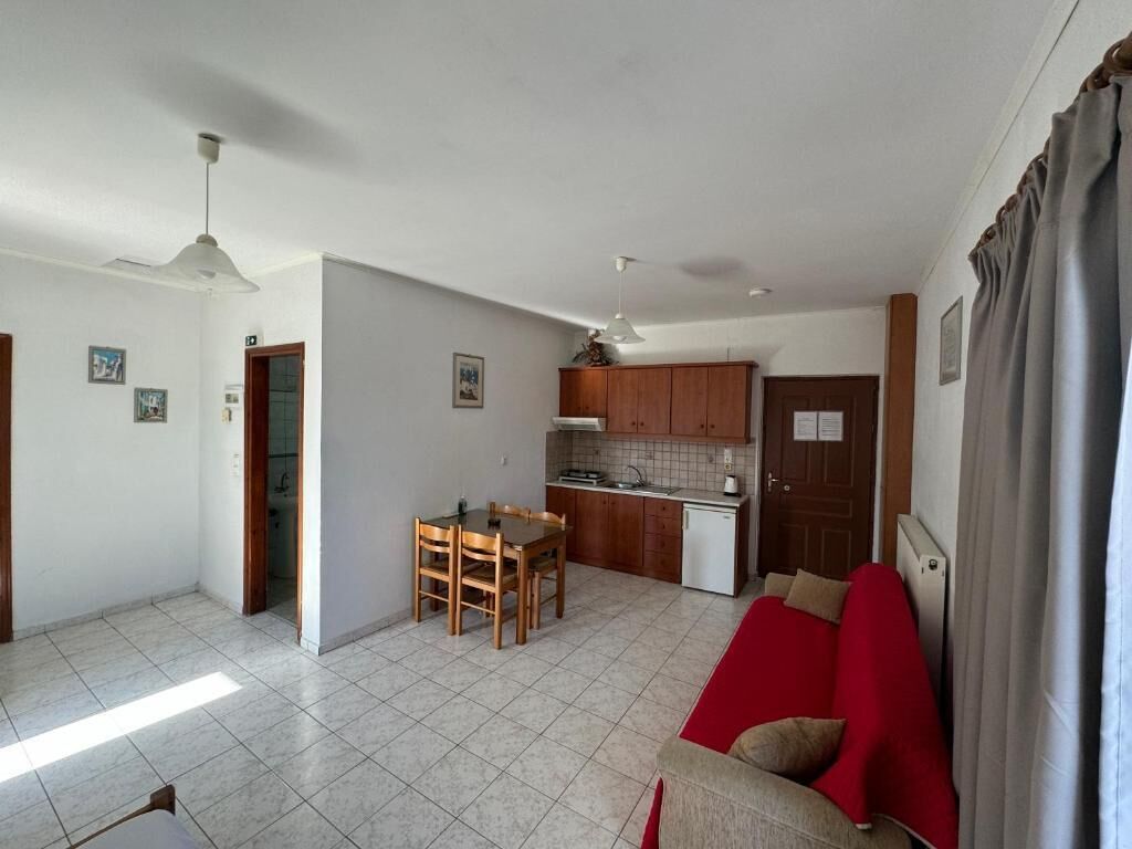 A living room with a red sofa, a dining area with a table and chairs, a kitchen with wooden cabinets and a white dishwasher, and a ceiling fan.