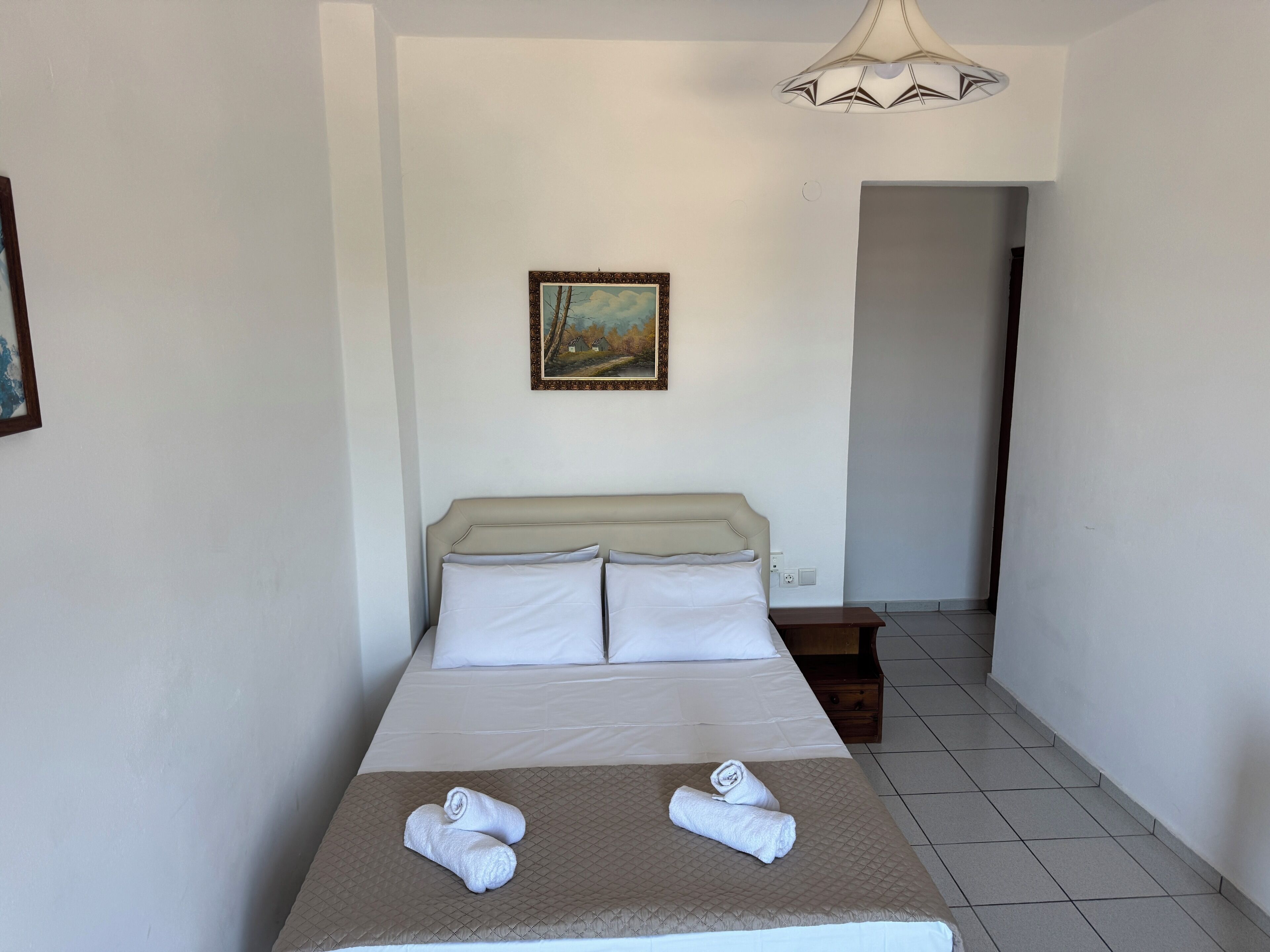 A hotel room with a bed, a painting on the wall, and a hallway.