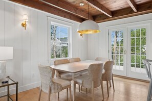 A dining area with a white table and wicker chairs, large windows, and a wooden ceiling. - Walk to Beach|Sleeps 10| Fire Pit|Hot Tub| Games (Kennebunk)