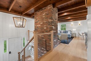 A staircase with wooden railings leading to a living area with a brick fireplace, a sofa, and a dining table. - Walk to Beach|Sleeps 10| Fire Pit|Hot Tub| Games (Kennebunk)