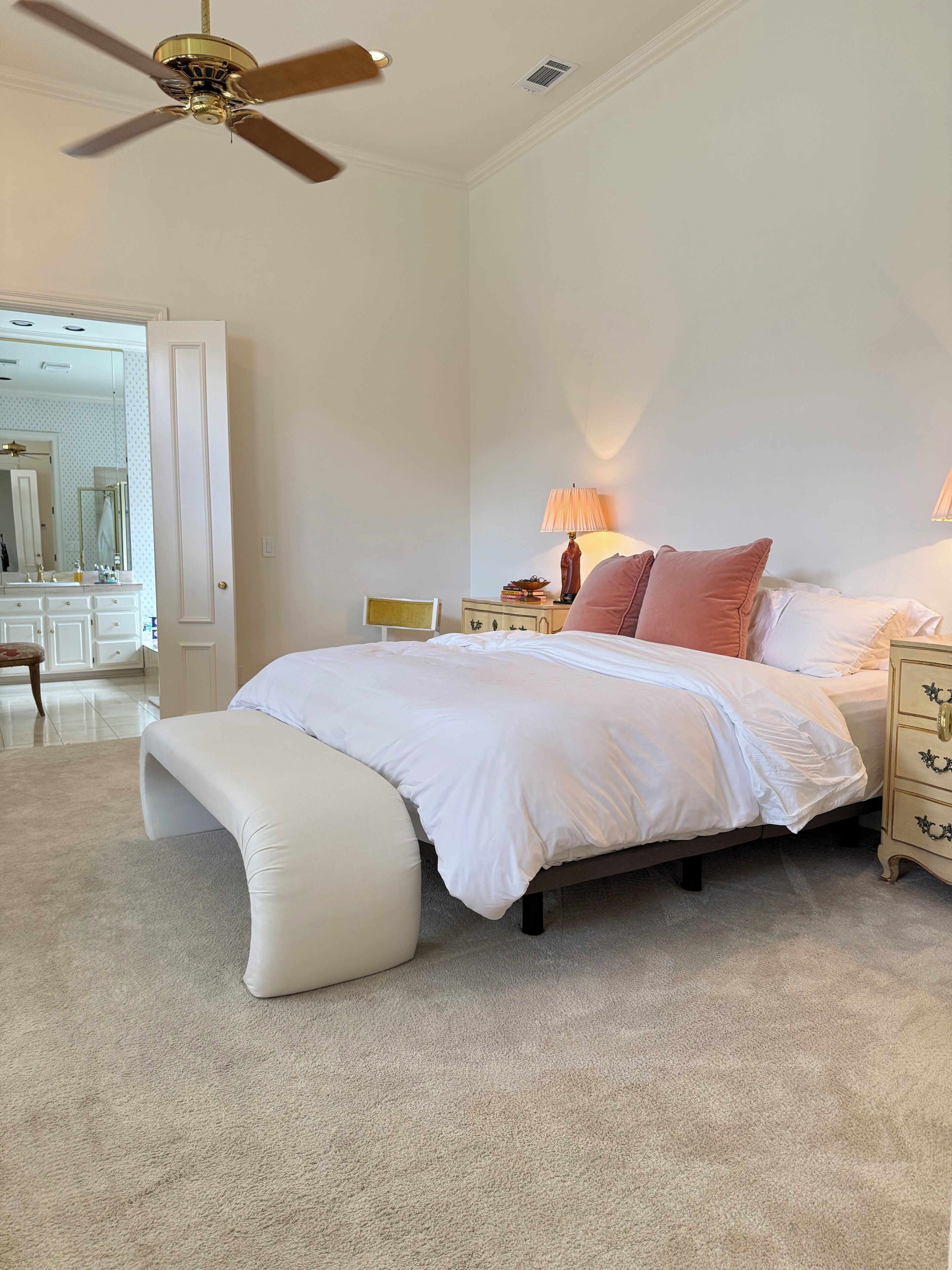 A bedroom with a bed, a bench, a nightstand, a lamp, a ceiling fan, and a mirror.