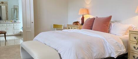 A bedroom with a bed, a bench, a nightstand, a lamp, a ceiling fan, and a mirror.