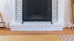Ein weißer Kamin aus Backstein mit einem schwarzen Bildschirm, ein gerahmtes Gemälde darüber und eine Ablage mit Kleinigkeiten.