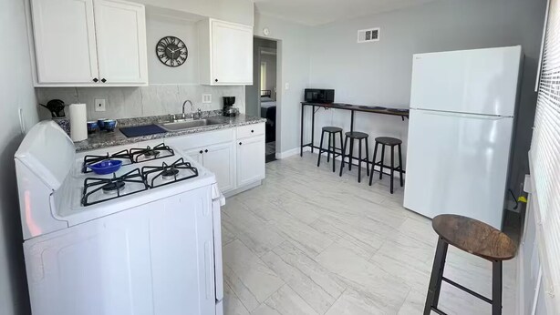 A kitchen with white cabinets, a gas stove, a sink, a microwave, and a refrigerator.