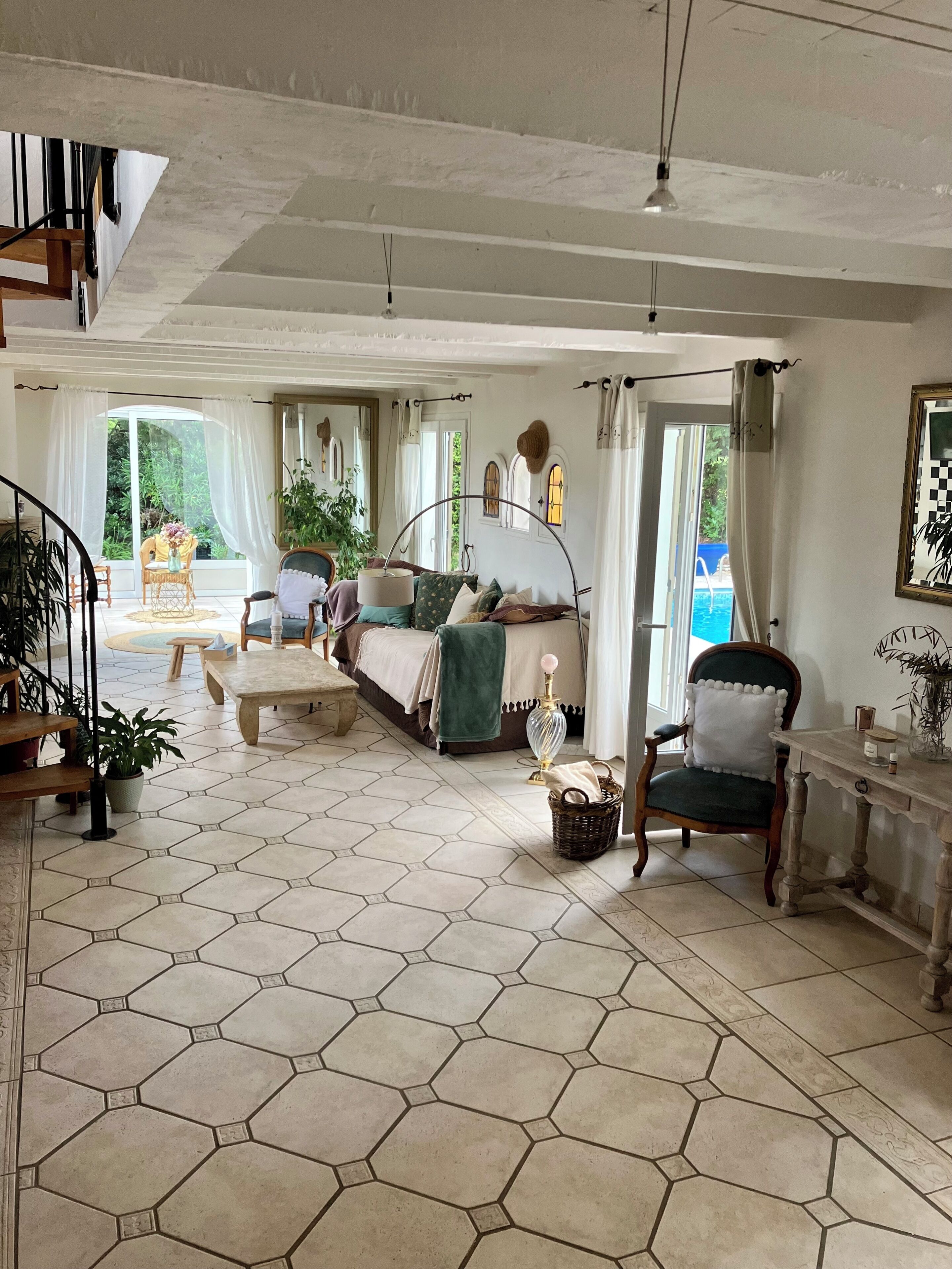 A spacious room with a large bed, a chair, a table, and a view of a pool through a window.