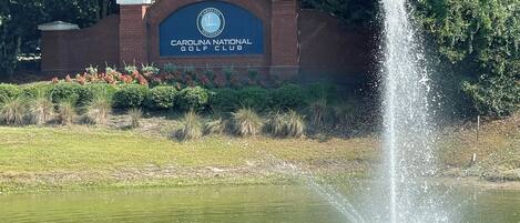 A sign for Carolina National Golf Club with a water fountain in the foreground.