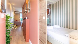 Moderni hotellihuone, jossa on puulattia, valkoisilla lakanoiden peitetty sänky, suuri peili ja ruukussa oleva kasvi.