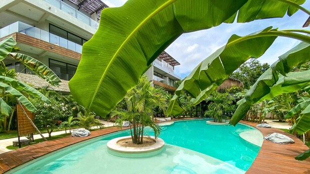 A modern pool with a wooden deck, surrounded by tropical plants and a building with large windows. - Tulum Style Escape | Private Pool & Nature Vibes (Tulum)