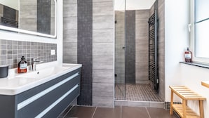 A modern bathroom with a large mirror, a sink, a shower with a glass door, and a wooden bench. - Daisy – Élégant cocon au cœur de Biarritz (Biarritz)