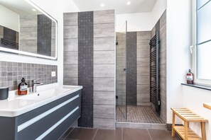 Ein modernes Badezimmer mit großem Spiegel, Waschbecken, Dusche mit Glastür und Holzbank.