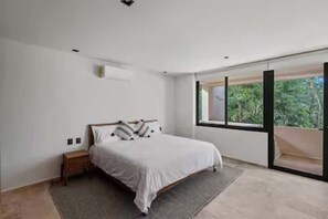 Ein Schlafzimmer mit Bett, Nachttisch, Fenster und Blick auf Grünfläche.