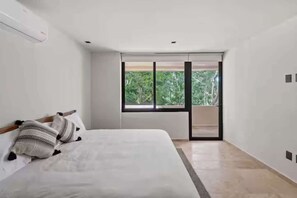 A bedroom with a bed, a window, and a view of greenery outside. - Chic Jungle 2BR - Balcony, Priv Pool, Steam & Gym (Tulum)