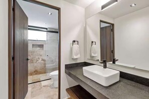 A modern bathroom with a large mirror, a white sink, and a shower area. - Chic Jungle 2BR - Balcony, Priv Pool, Steam & Gym (Tulum)