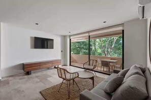 A modern living room with a flat-screen TV, a sofa, a coffee table, and a dining area with chairs. - Chic Jungle 2BR - Balcony, Priv Pool, Steam & Gym (Tulum)