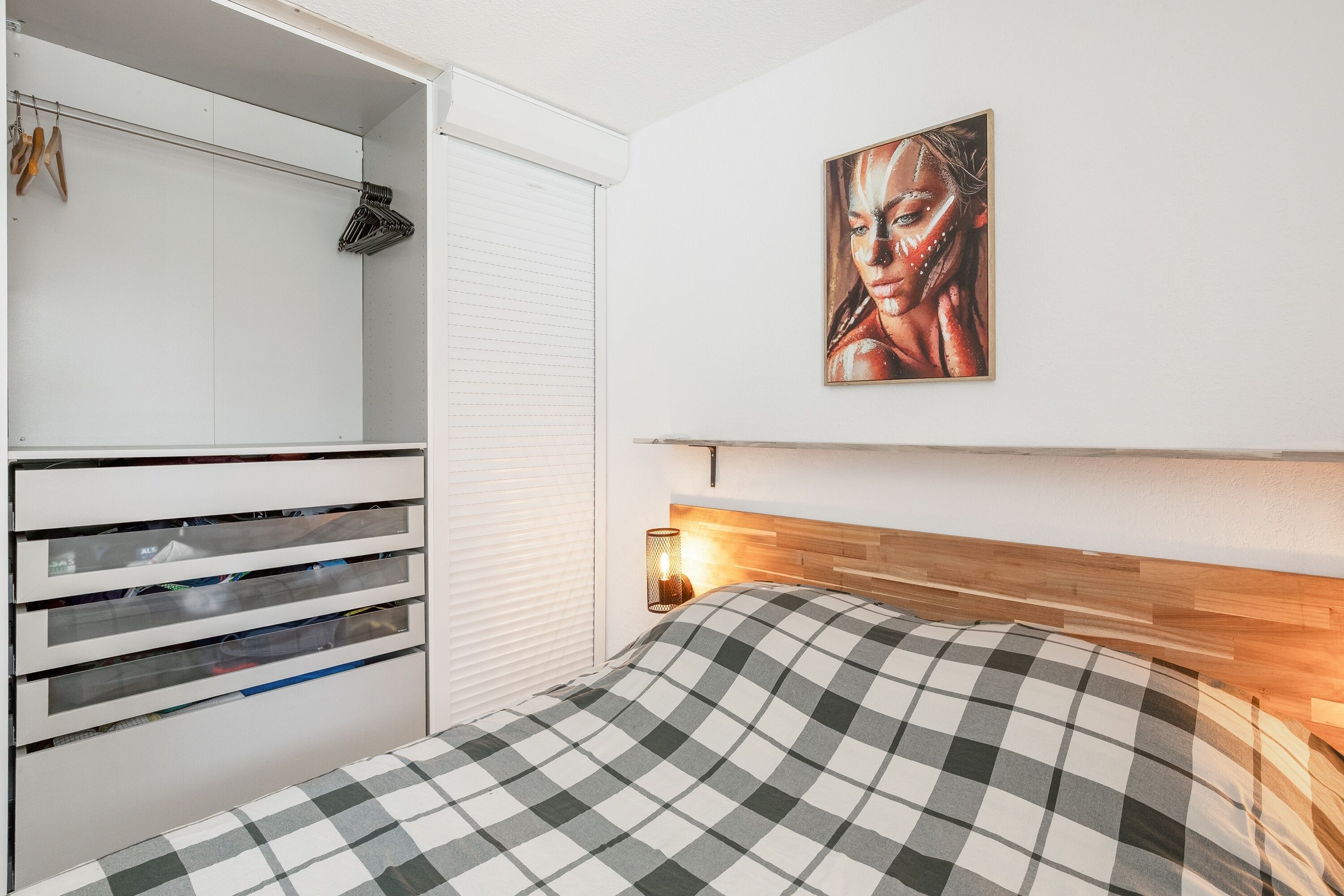 A bedroom with a bed, a wardrobe, a painting on the wall, and a bedside lamp.
