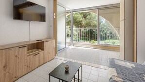 Ein modernes Zimmer mit einem Holzkasten, einem kleinen Tisch mit einer Tasse und einer großen Glasschiebetür, die auf einen Balkon mit Blick auf Bäume führt.
