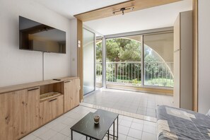 Ein modernes Zimmer mit einem Holzkasten, einem kleinen Tisch mit einer Tasse und einer großen Glasschiebetür, die auf einen Balkon mit Blick auf Bäume führt.