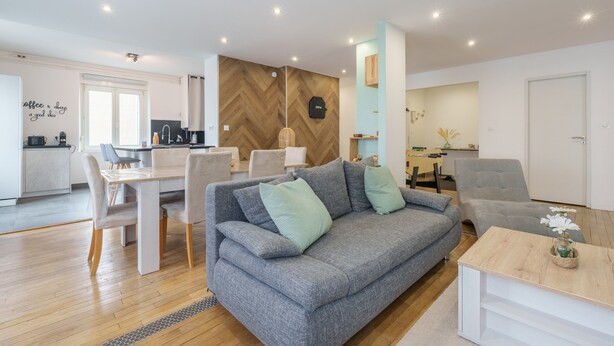 Una sala moderna con un sofá gris, una mesa de comedor y una cocina al fondo.