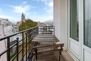 Ein Balkon mit einer hölzernen Bank, einem Metallgeländer und Blick auf eine Kirche sowie Gebäude in der Ferne.