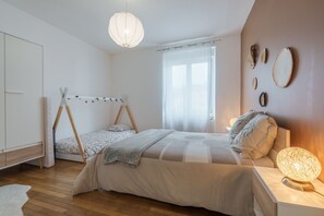 Ein Schlafzimmer mit Bett, einer Pendelleuchte, einem Fenster mit Vorhängen und Wanddekoration.