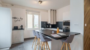 Una cocina moderna con una isla central, taburetes de bar, una cafetera y un ventanal.