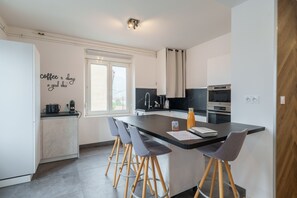 Eine moderne Küche mit einer zentralen Kochinsel, Barhocker, einer Kaffeemaschine und einem Fenster.