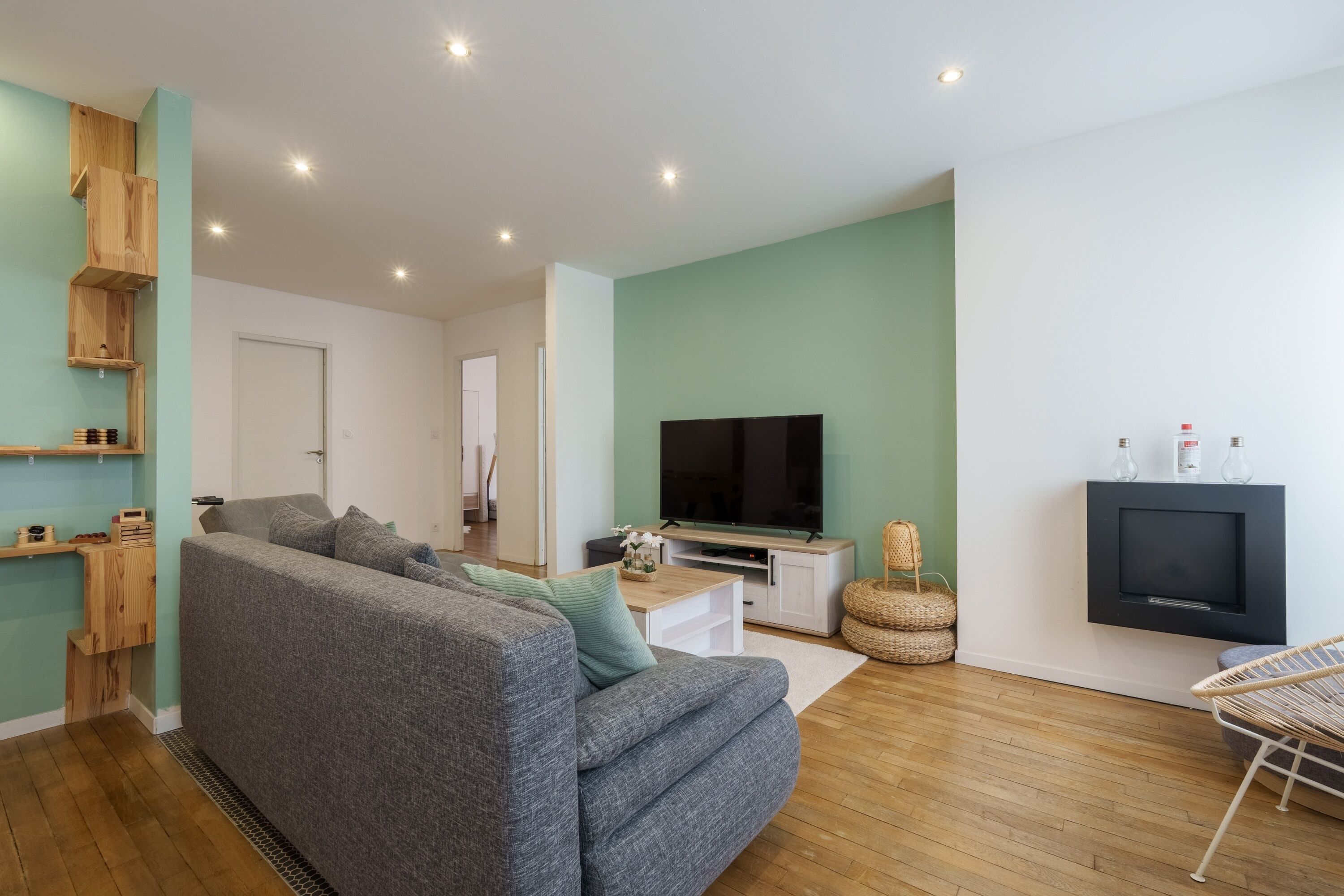 Ein Wohnzimmer mit grauem Sofa, Holzregalen, einem Fernseher und einem Kamin.
