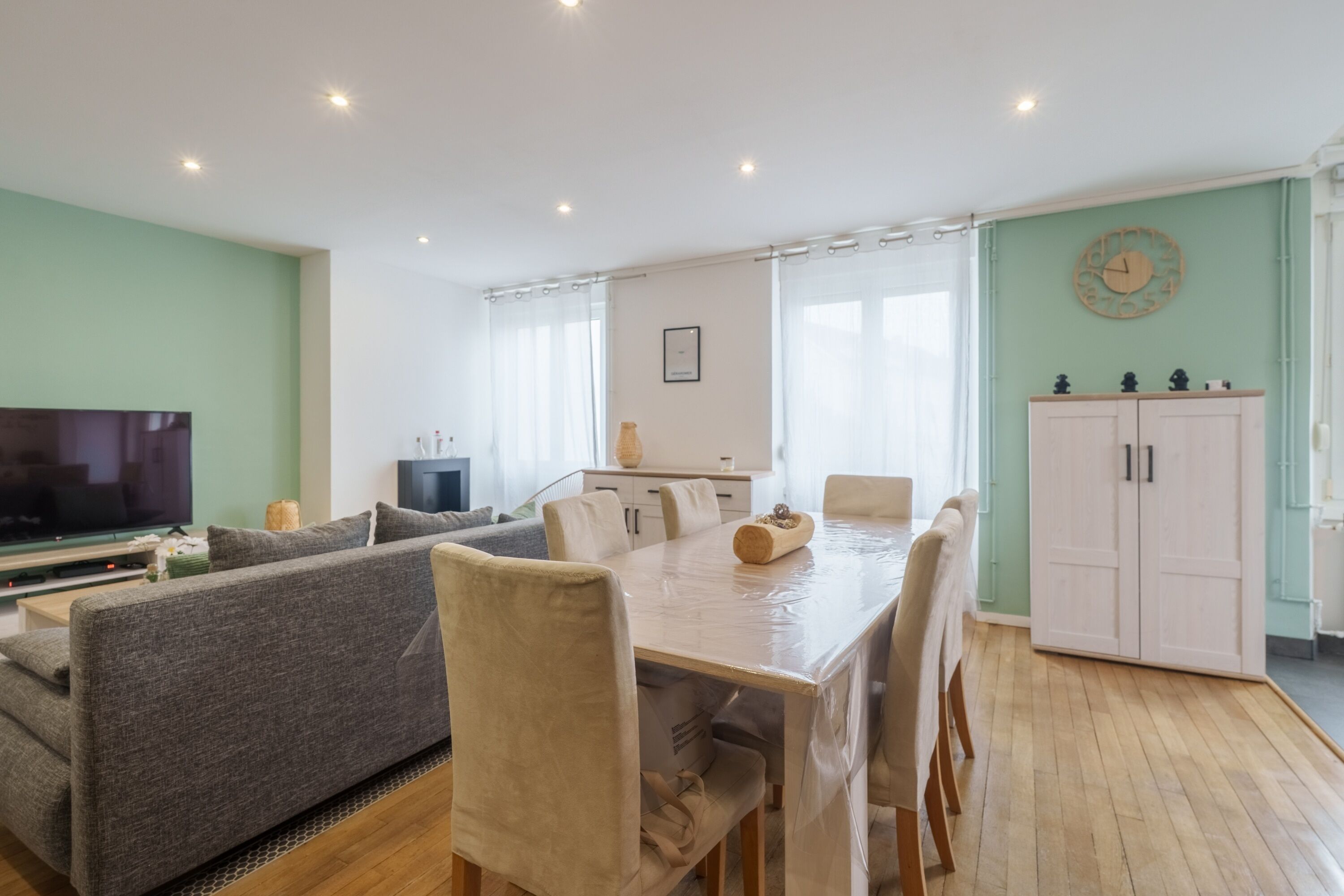 A modern living room with a sofa, dining table, chairs, a TV, and a cabinet.