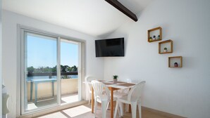 Una habitación con puerta de vidrio corredera que da a un balcón, un televisor de pantalla plana montado en la pared y tres pequeños cuadros enmarcados.