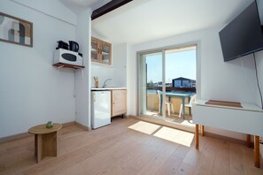 Eine moderne Küche mit Mikrowelle, Kühlschrank und Holzschränken. Ein kleiner Tisch mit einer Vase und ein Stuhl stehen dort. Ein großes Fenster bietet einen Blick nach draußen.