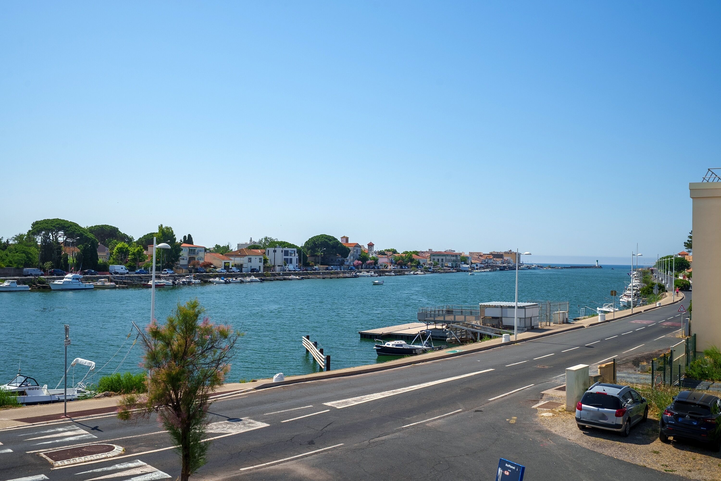 Una strada costiera con un porto turistico, imbarcazioni ed edifici lungo l'acqua.