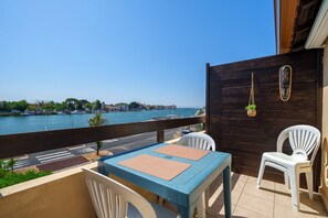 Ein Balkon mit Blick auf ein Gewässer, einem Tisch mit Stühlen und einer hängenden Pflanze.