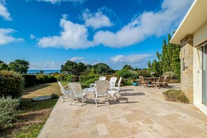 Eine Terrasse mit Gartenmöbeln, einer Steinsäule und Blick auf das Meer.