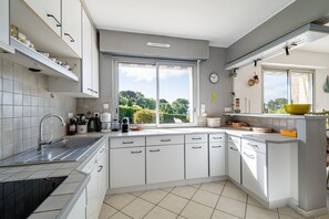 Eine moderne Küche mit weißen Schränken, einem großen Fenster und Blick ins Grüne.